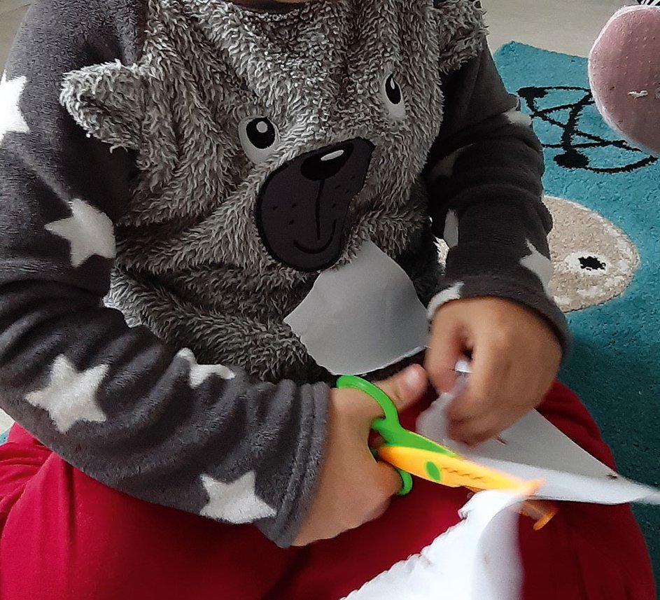 Kinde schneidet bei der Frühförderung mit einer Kinderschere ein Blatt Papier.