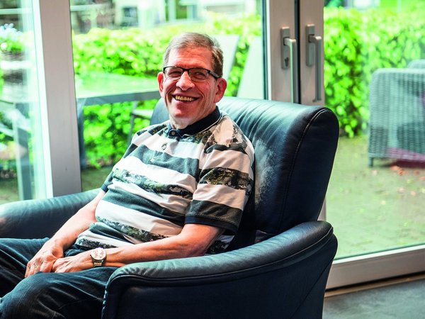 Ein Mann mit Behinderung sitzt in einem Sessel in einer Wohneinrichtung und lächelt