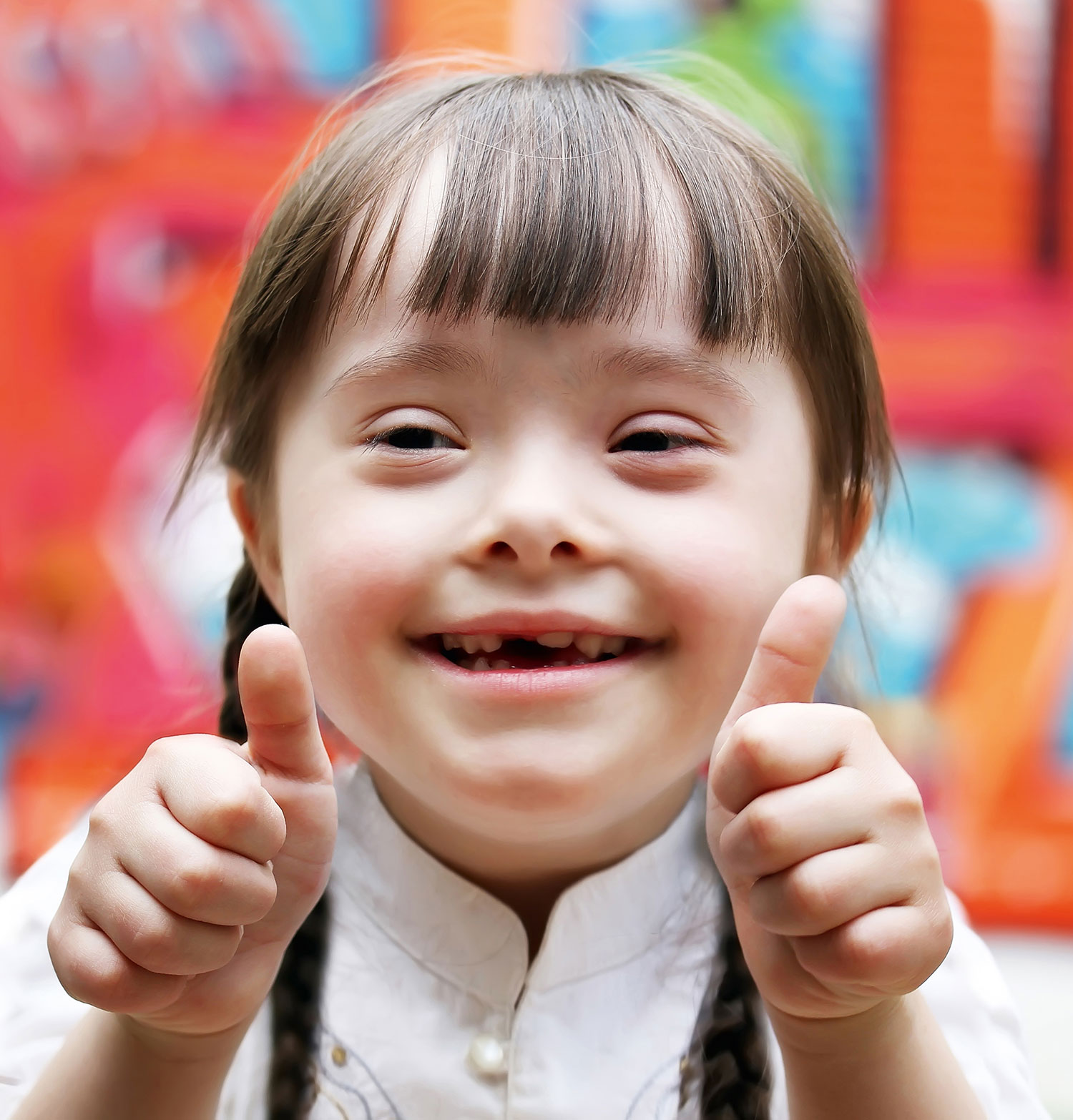Ein Mädchen mit Behinderung hebt lächelnd ihre beide Daumen in die Luft. 