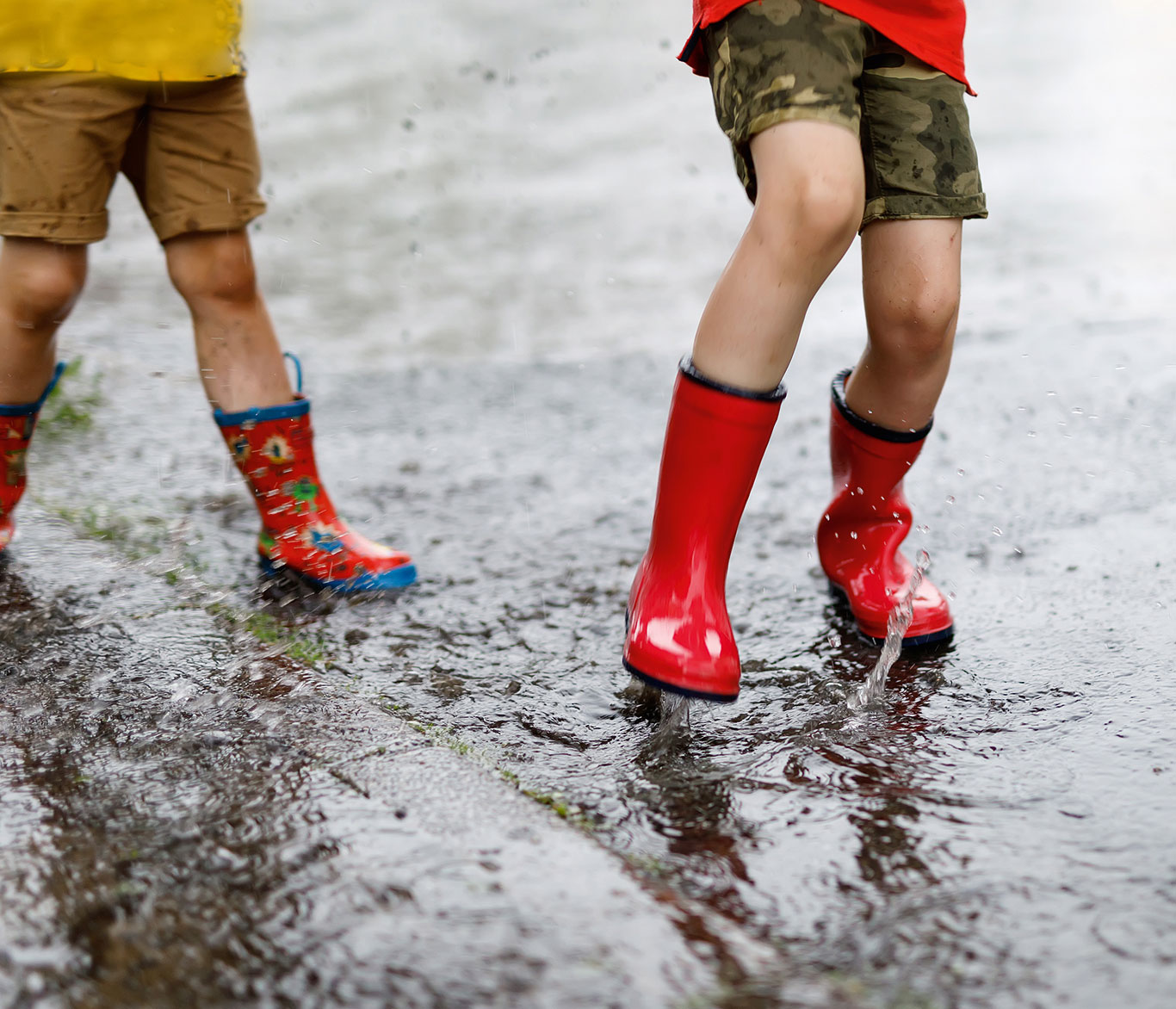 Zwei Kinder einer Tagesgruppe spielen in Gummistiefeln draußen im Regen.