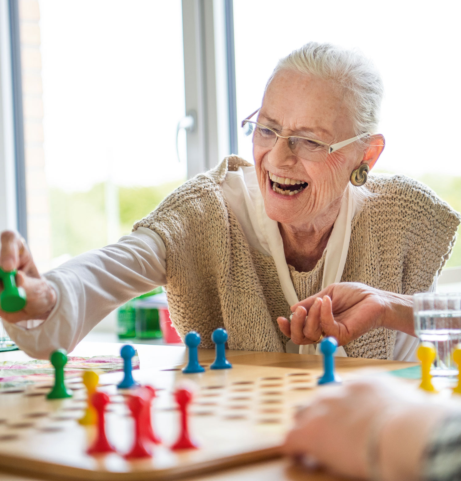 Eine Seniorin spielt in der Tagespflege der Vorwerker Diakonie ein Brettspiel und lacht.