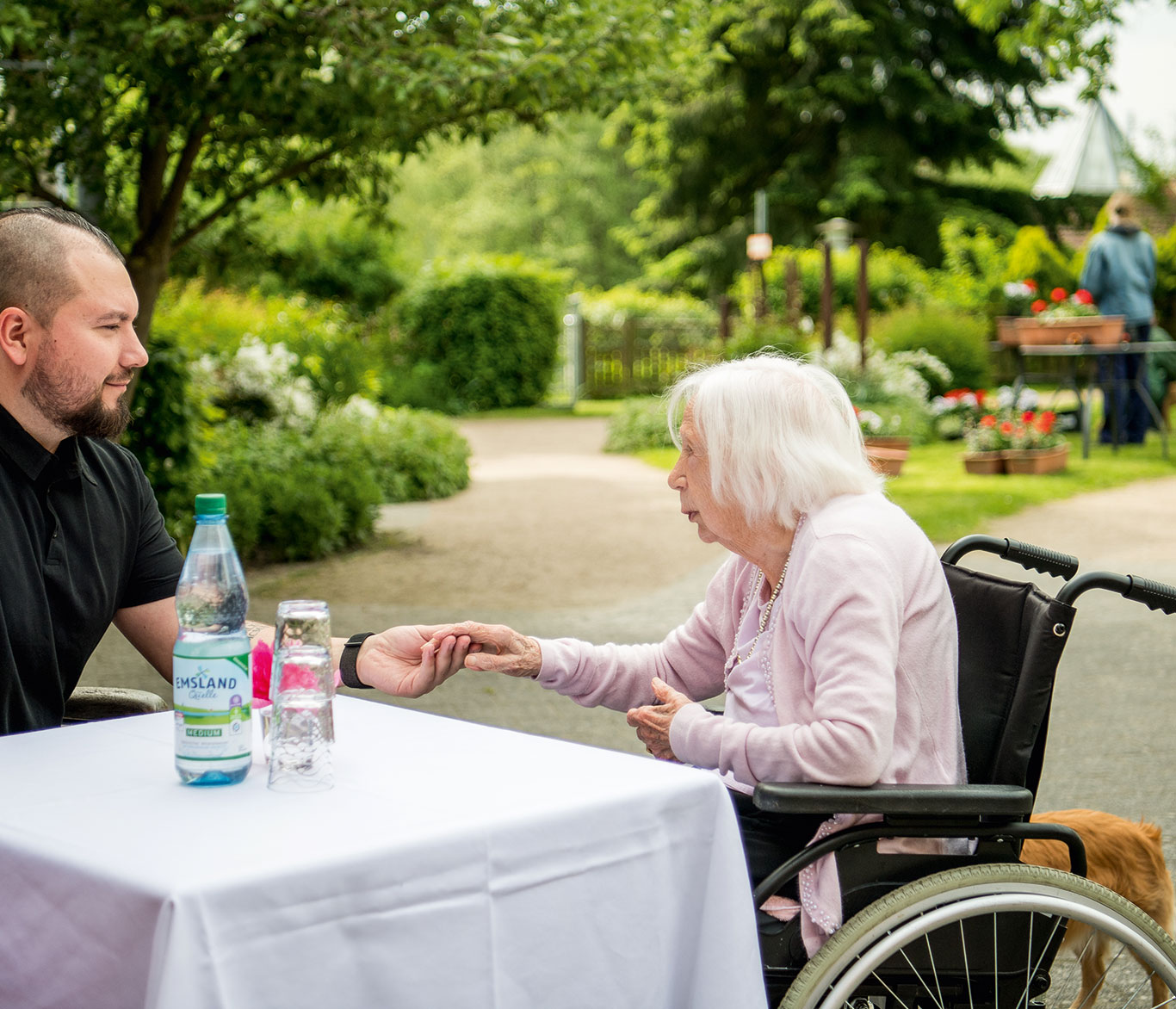 Ein Pfleger hält am Tisch die Hand einer an Demenz erkrankten Seniorin.