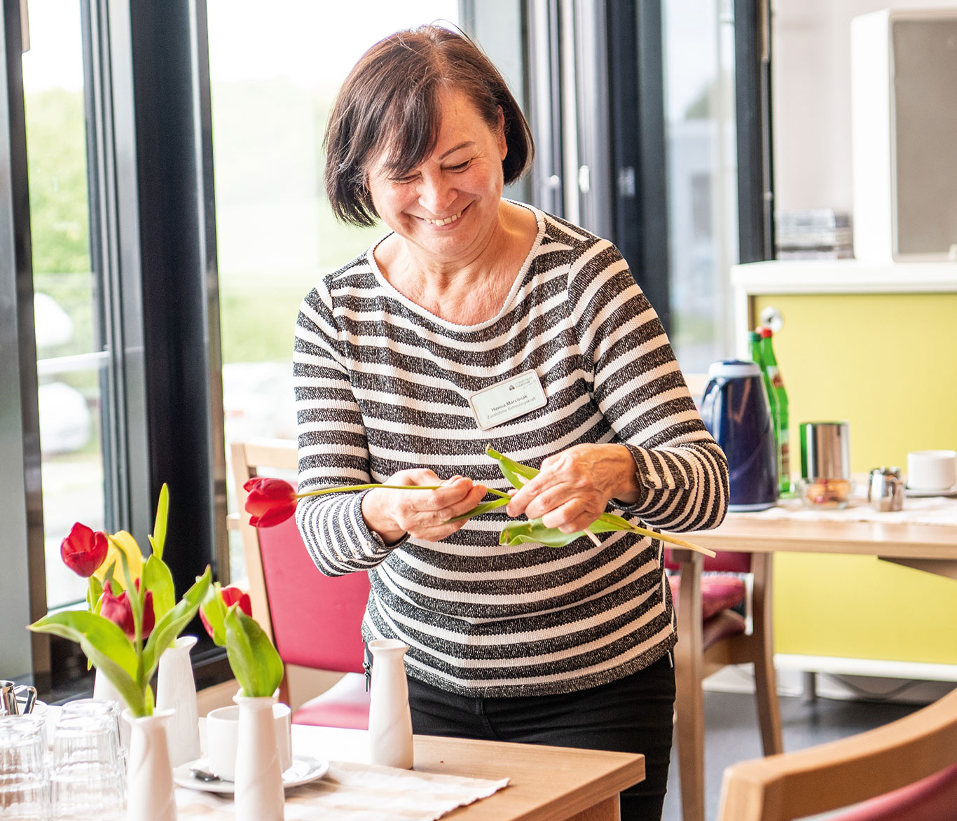 Eine Mitarbeiterin der Einrichtung der Seniorenpflege in Travemünde dekoriert einen Tisch mit Blumen..