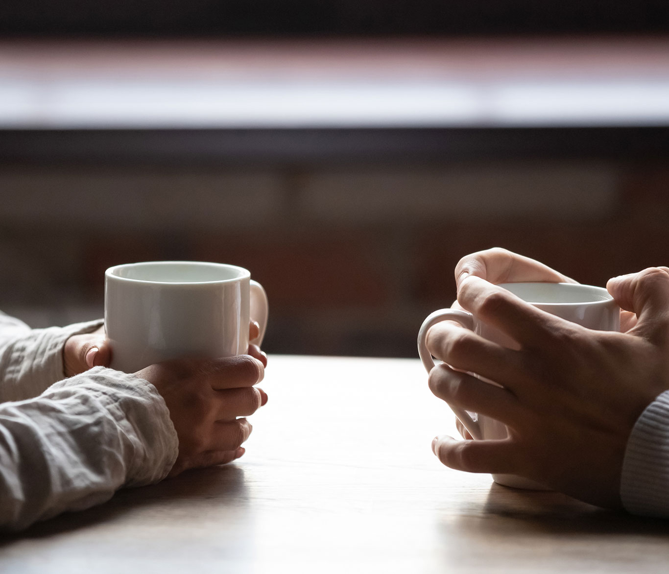 Zwei Menschen sitzen sich mit Kaffeetassen an einem Tisch gegenüber.