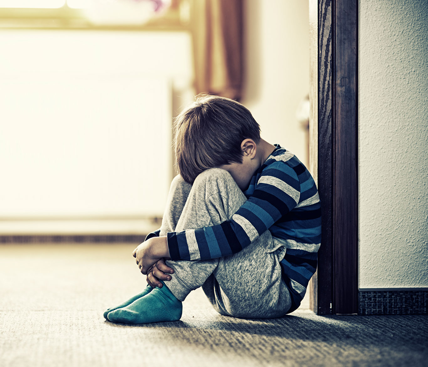 Ein Junge sitzt zusammengekauert auf dem Fußboden vor einer Wand.