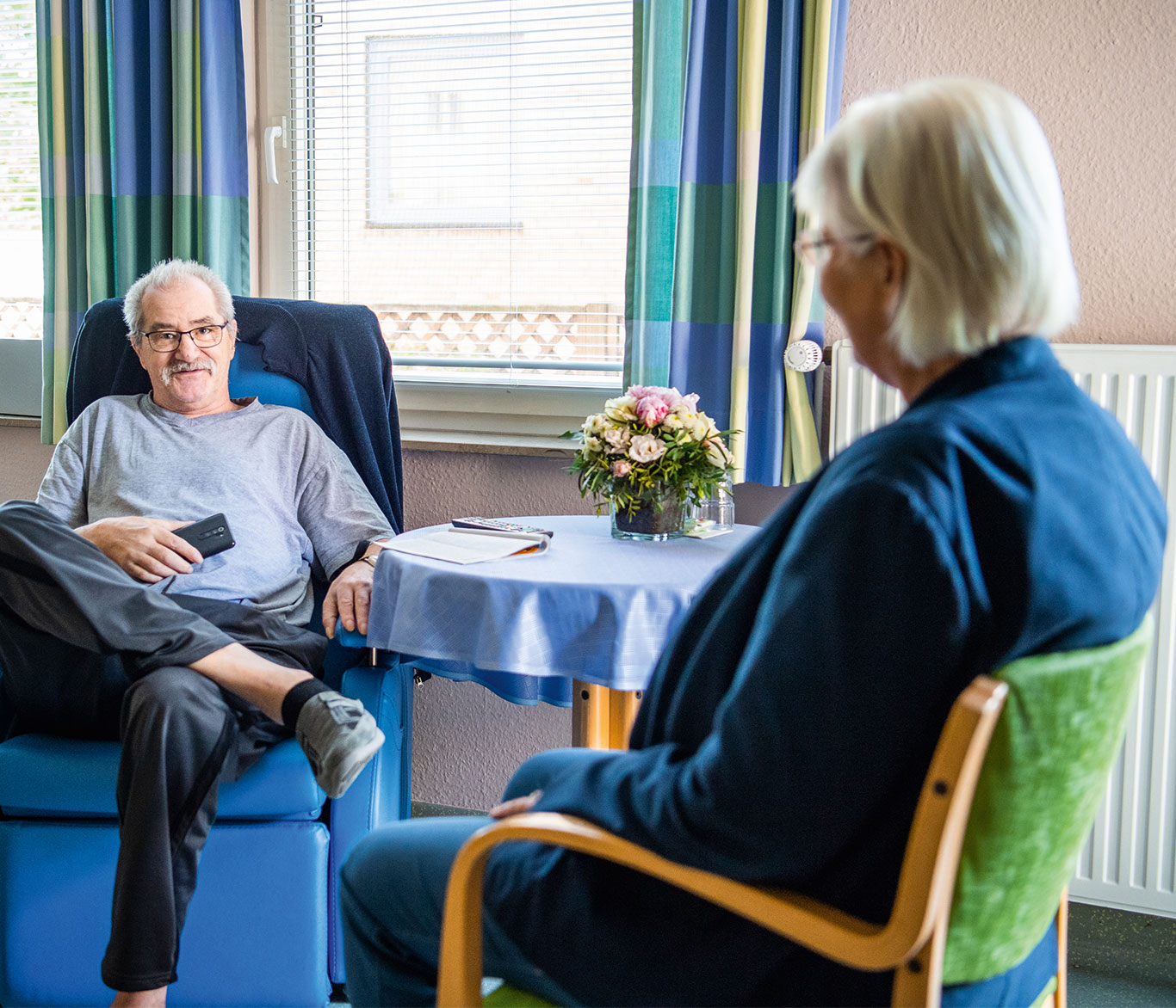 Eine Mitarbeiterin des Hospiz in Lübeck unterhält sich mit einem Gast in seinem Zimmer.