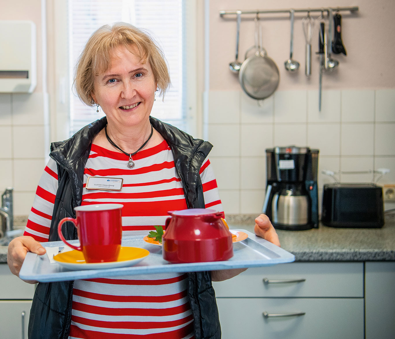 Eine ehrenamtliche Mitarbeiterin des Hospiz in Lübeck hält ein Tablett mit einer Kanne und einer Tasse. 