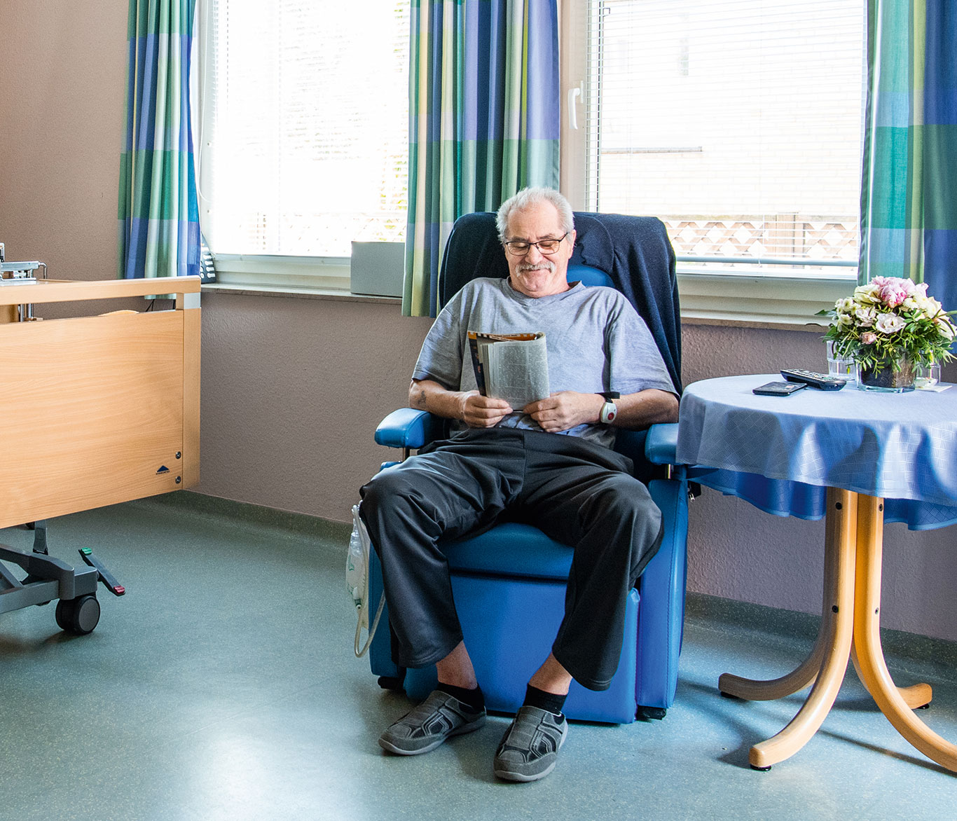 Ein Mann liest in seinem Zimmer im Hospiz der Vorwerker Diakonie in seinem Sessel eine Zeitschrift.