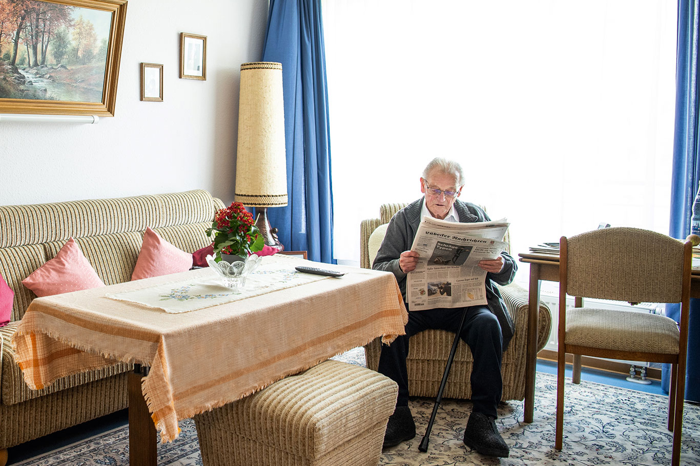 Pflegebedürftiger Senior liest im Zimmer der Einrichtung der Seniorenpflege Zeitung.